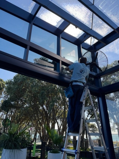 Urban Exterior cleaner on a ladder cleaning the glass canopy of a waterfront commercial building