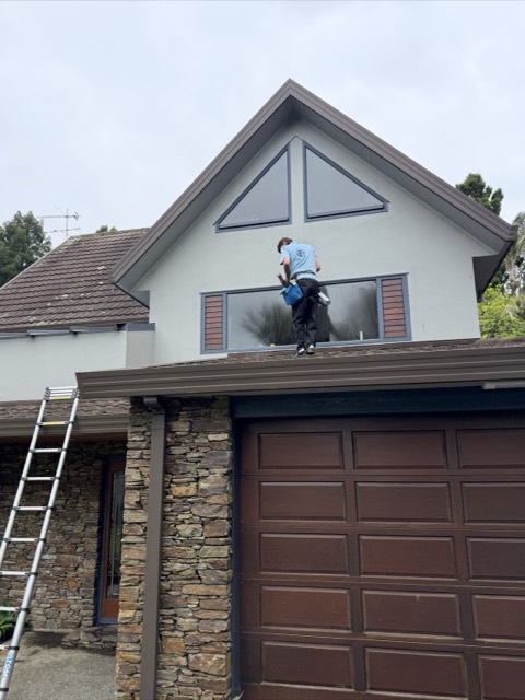 Urban Exterior cleaner on a roof cleaning the gable window of a two-storey home