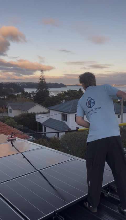 Cleaning rooftop solar panels at sunset with the harbour behind